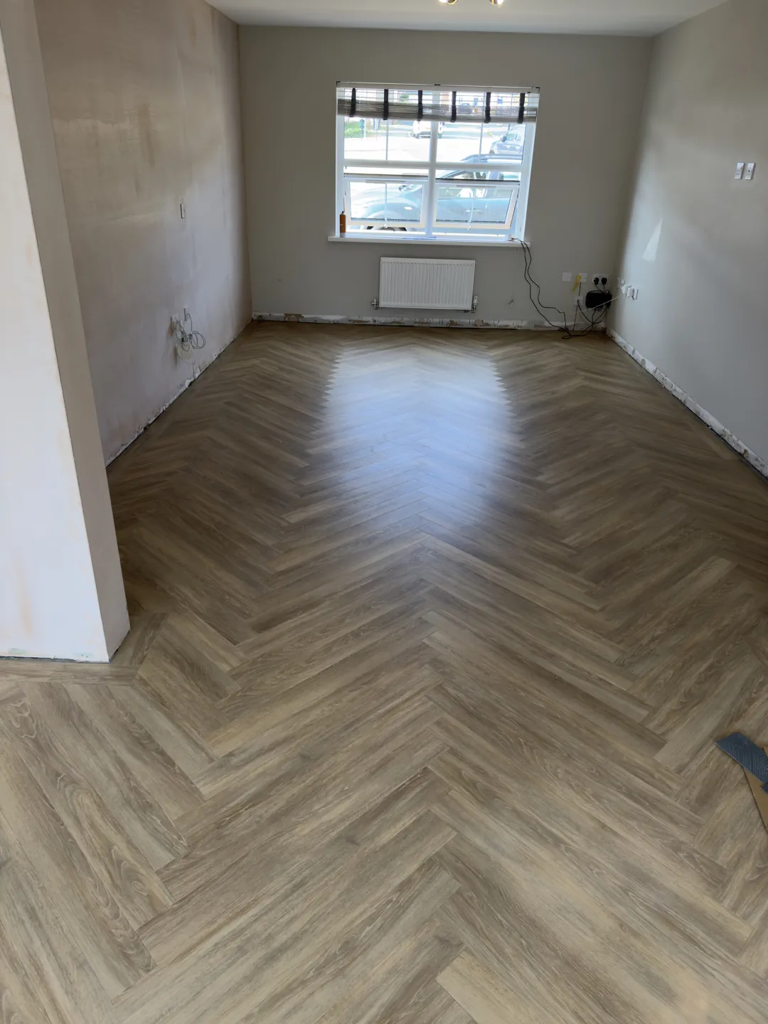 Herringbone wood-effect floor laid across an empty room towards a window